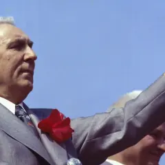 Edward Gierek, wznosząc rękę, symbolizuje czasy, gdy starał się budować Polskę, inwestując w rozwój przemysłu i poprawę bytu obywateli.