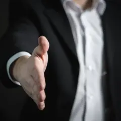 Mężczyzna w garniturze wyciąga rękę do uścisku, gotowy do przedstawiania się po niemiecku, pytań i odpowiedzi.