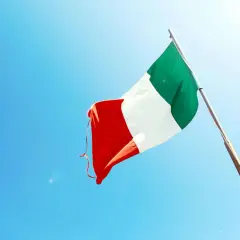 Włoska flaga powiewa na tle błękitnego nieba. Czy język włoski jest trudny? Może nauka będzie łatwiejsza, gdy będziesz marzyć o słonecznych Włoszech.