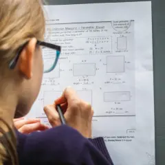 Dziewczynka w okularach rozwiązuje zadania z matematyki w praktyce, obliczając obwody prostokątów.