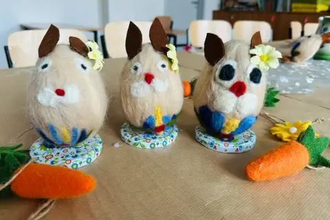 Trzy filcowe zajączki, ozdobione kwiatkami i kolorowymi spódniczkami, jakby mówiły po kaszubsku. Obok leżą filcowe marchewki.