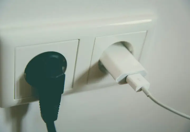 Gniazdko elektryczne z podłączoną czarną wtyczką i białym adapterem USB. Wzór na napięcie skuteczne jest kluczowy dla bezpieczeństwa.