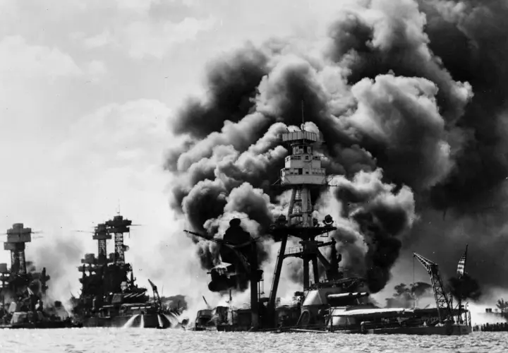 Okręty płoną po ataku, który był jedną z przyczyn ataku na Pearl Harbor. Dym zasnuwa niebo nad zatoką.