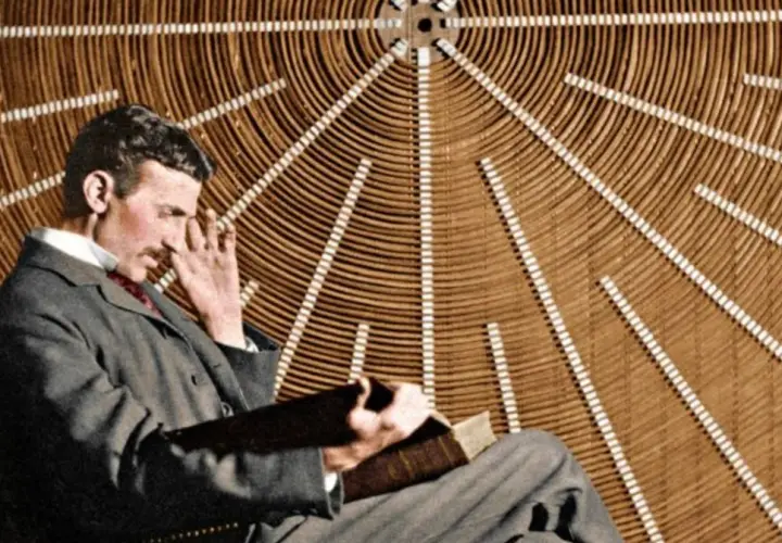 Nikola Tesla w okularach, zamyślony, siedzi przed aparaturą, która mogłaby być prototypem jego "promienia śmierci".