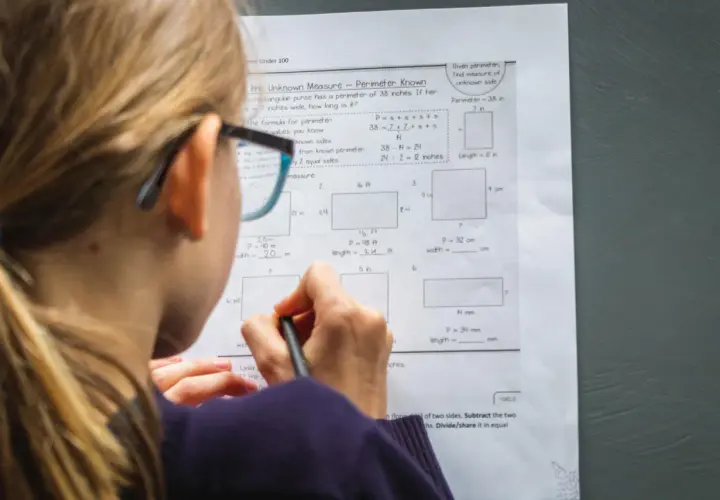 Dziewczynka w okularach rozwiązuje zadania z matematyki w praktyce, obliczając obwody prostokątów.