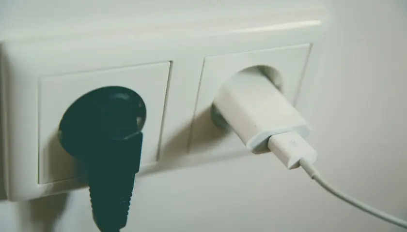 Gniazdko elektryczne z podłączoną czarną wtyczką i białym adapterem USB. Wzór na napięcie skuteczne jest kluczowy dla bezpieczeństwa.