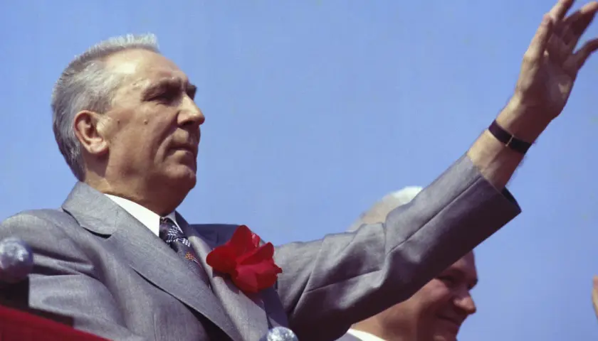 Edward Gierek, wznosząc rękę, symbolizuje czasy, gdy starał się budować Polskę, inwestując w rozwój przemysłu i poprawę bytu obywateli.