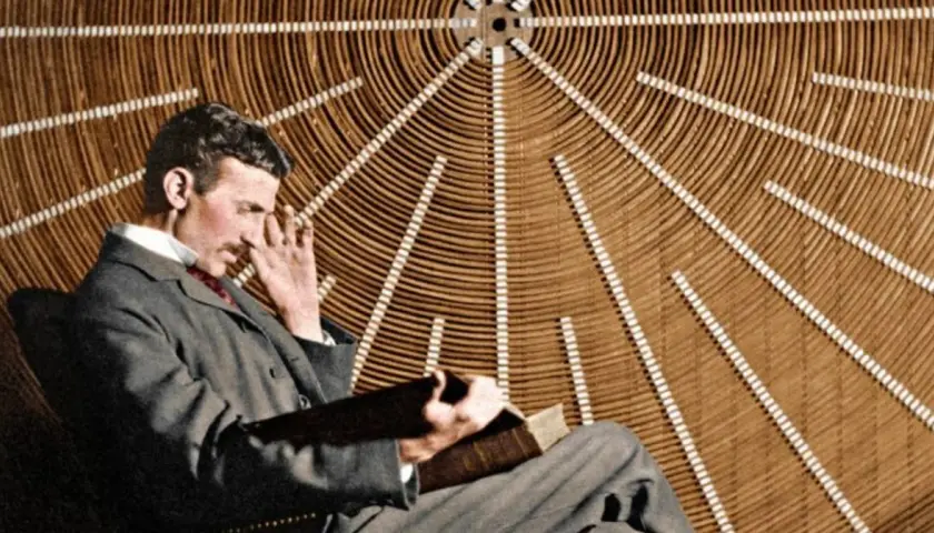 Nikola Tesla w okularach, zamyślony, siedzi przed aparaturą, która mogłaby być prototypem jego "promienia śmierci".