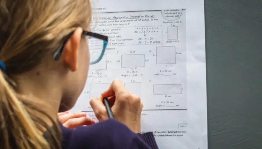 Dziewczynka w okularach rozwiązuje zadania z matematyki w praktyce, obliczając obwody prostokątów.