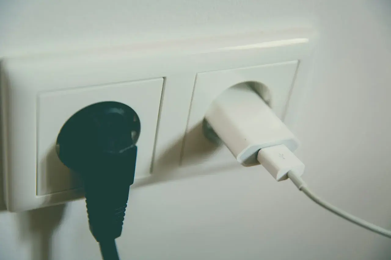 Gniazdko elektryczne z podłączoną czarną wtyczką i białym adapterem USB. Wzór na napięcie skuteczne jest kluczowy dla bezpieczeństwa.