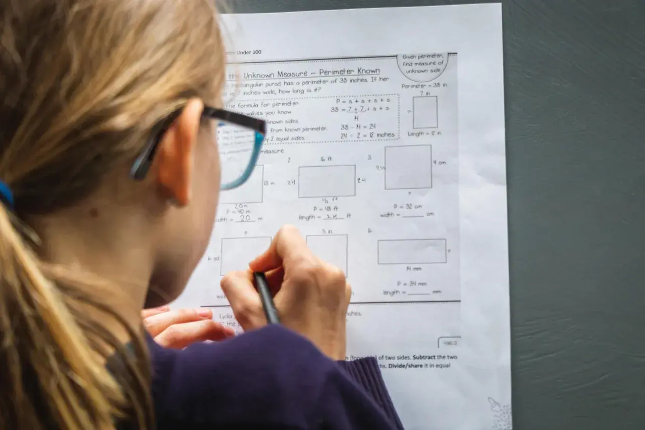 Dziewczynka w okularach rozwiązuje zadania z matematyki w praktyce, obliczając obwody prostokątów.