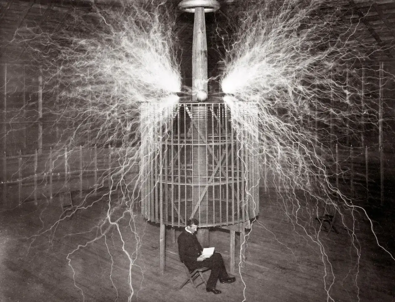 Nikola Tesla, otoczony błyskawicami, siedzi spokojnie przy swoim transformatorze. To jeden z jego genialnych wynalazków.