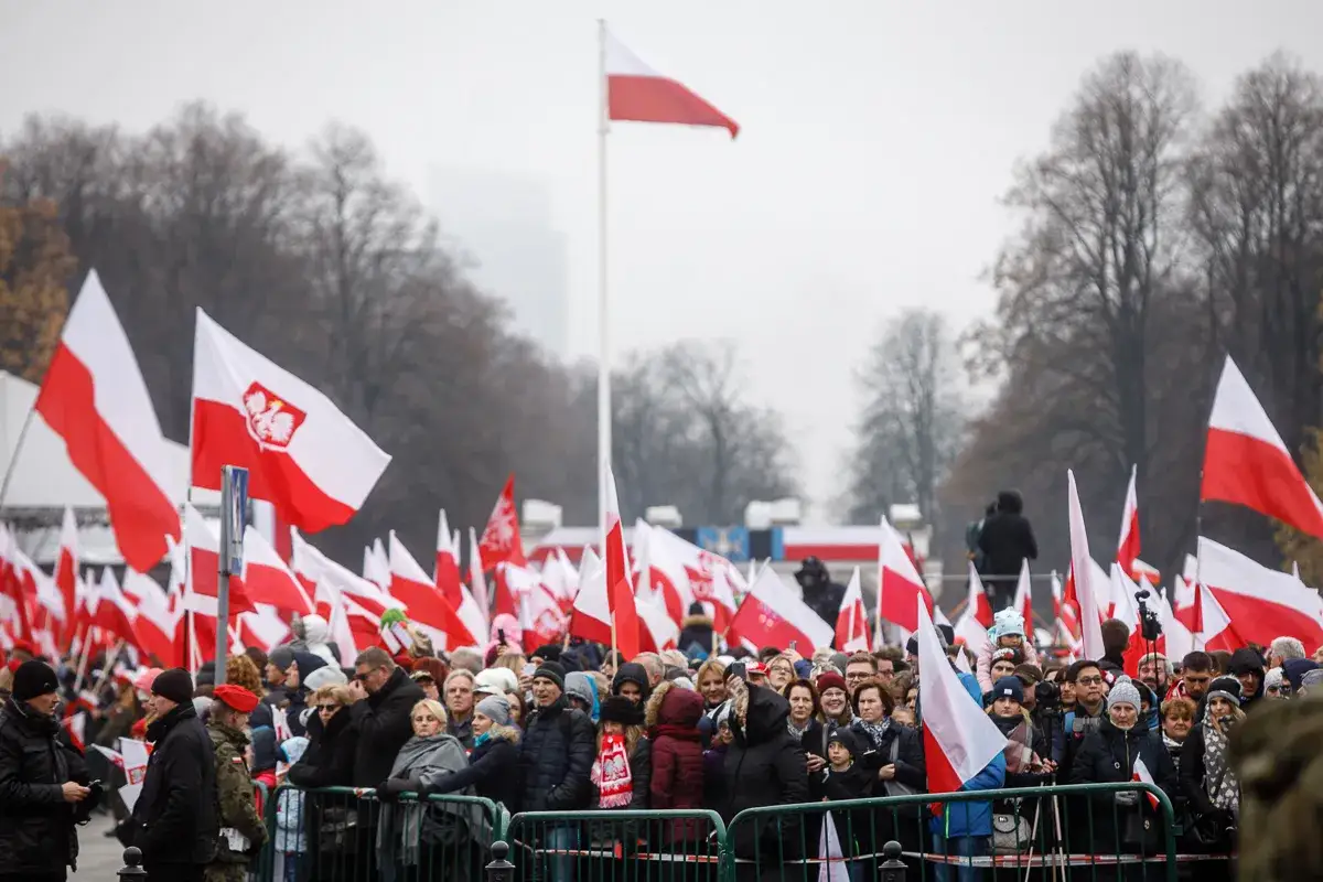 Tłum ludzi świętuje Dzień Niepodległości, machając polskimi flagami.