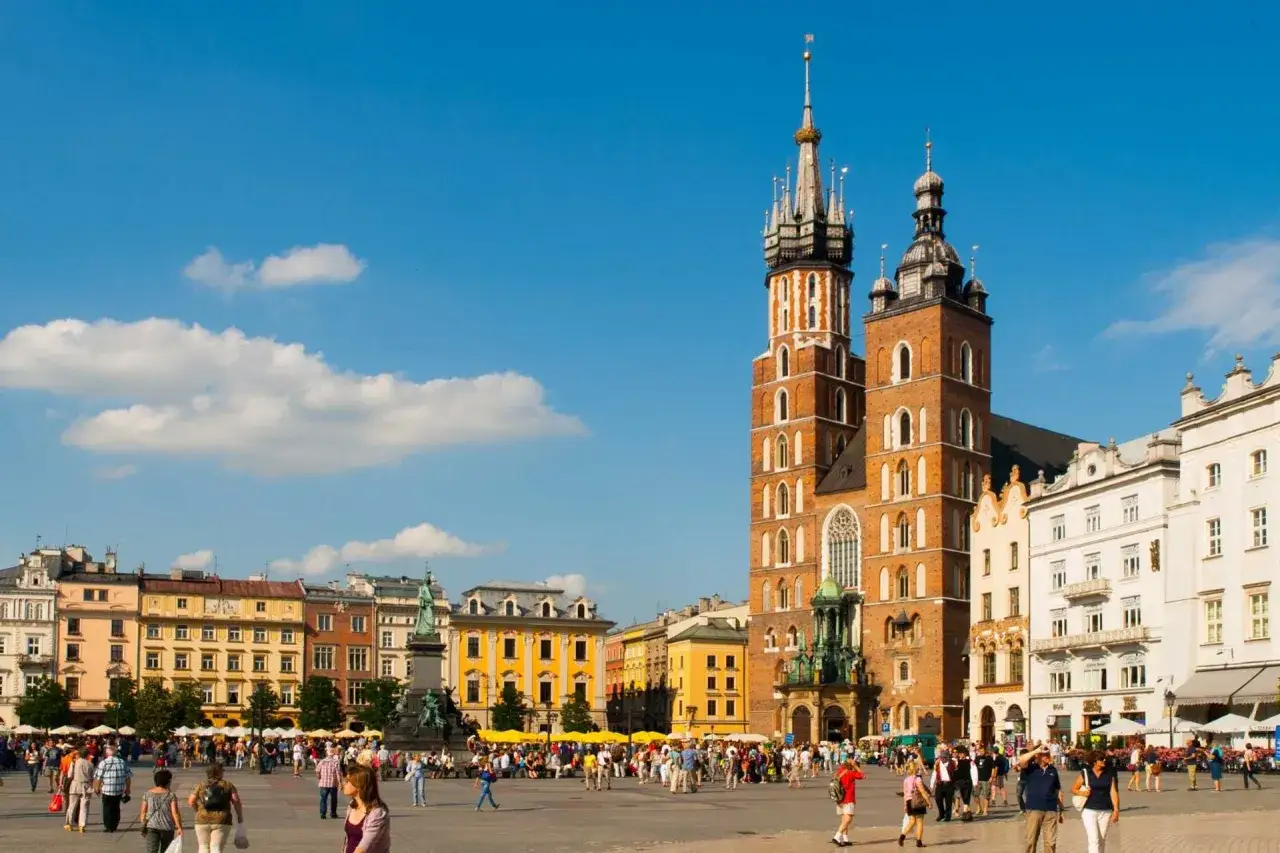 Rynek Główny w Krakowie, z Bazyliką Mariacką w tle. Tłumy ludzi spacerują po placu, zastanawiając się, ile lat ma Kraków.